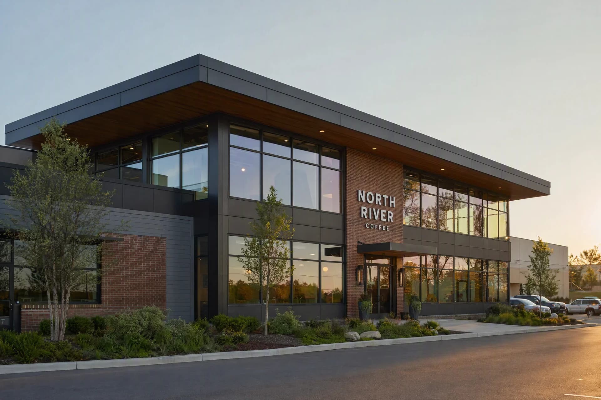 Two-storey brick and glass commercial building with trees and landscaped planting in evening light.
